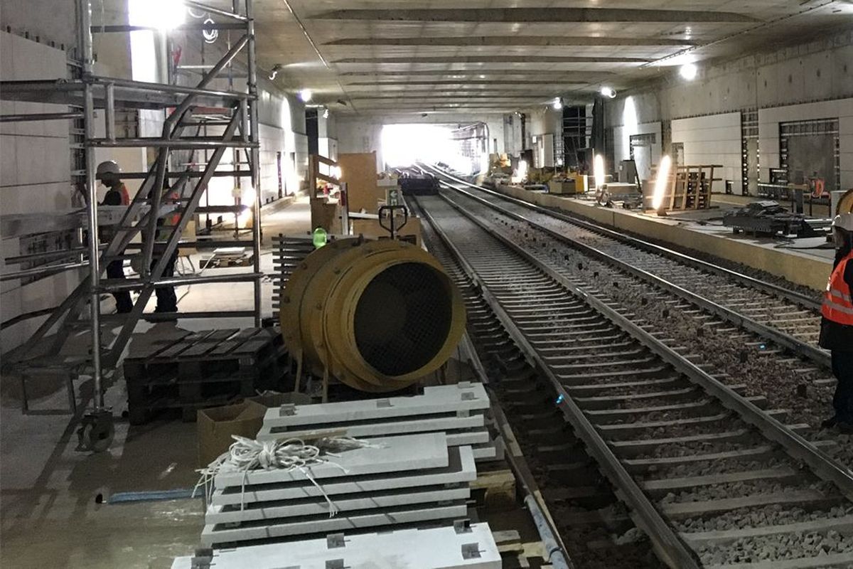 A construction worker stands on a railway track in a tunnel, surrounded by construction site materials and tools.