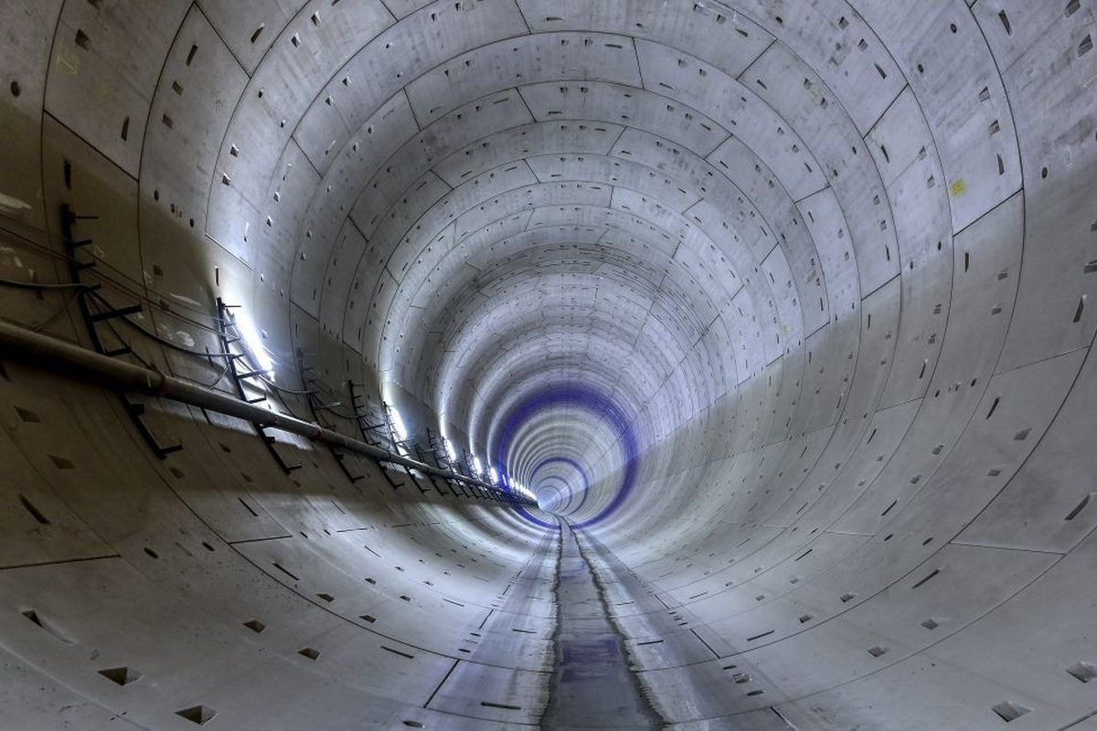 A view into a long, cylindrical tunnel with concrete walls and dim light at the end.