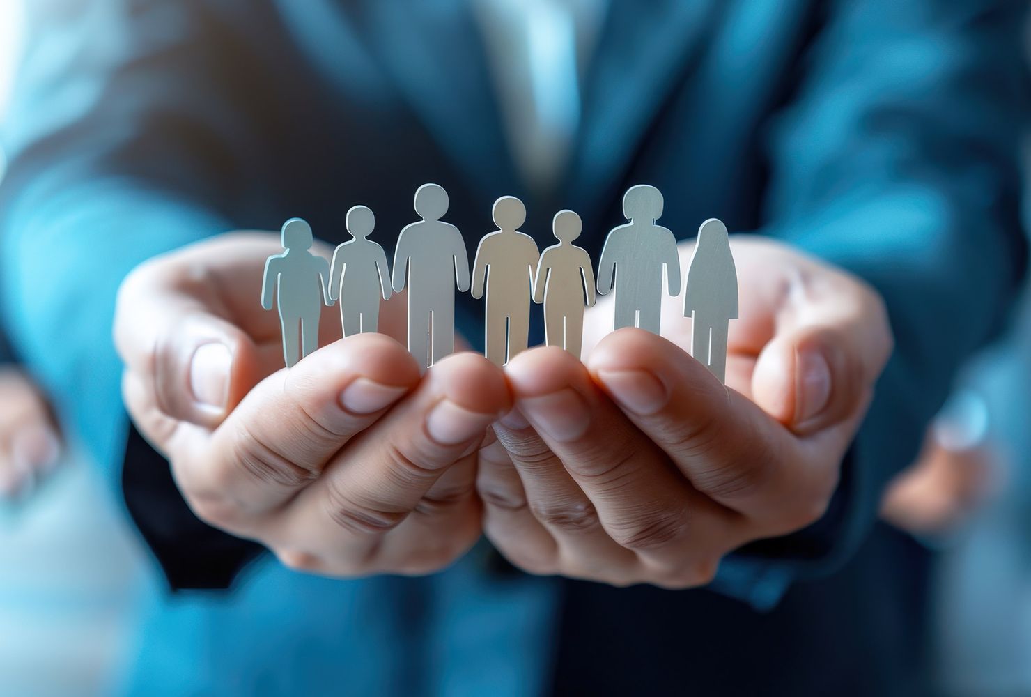 Two hands hold figures of people of different sizes, symbolising community and cooperation.