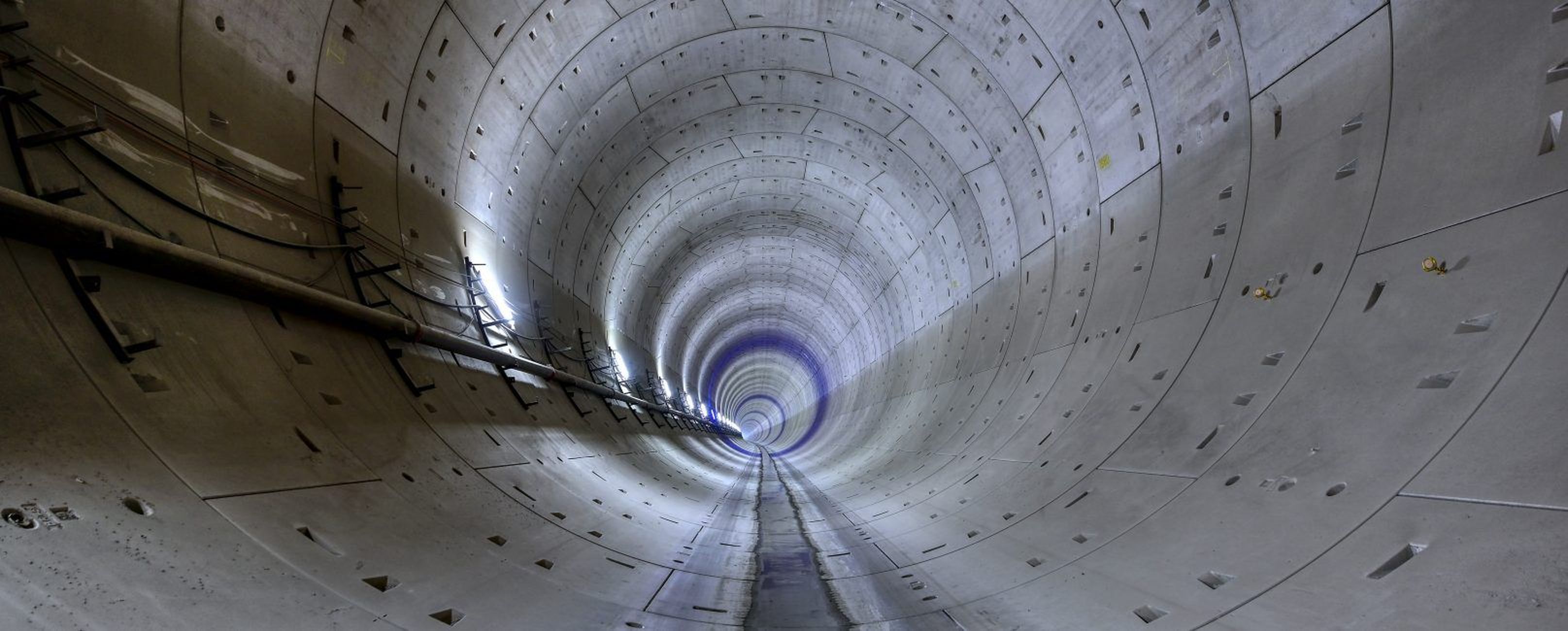 Ein Blick in einen langen, zylindrischen Tunnel mit Betonwänden und schwachem Licht am Ende.